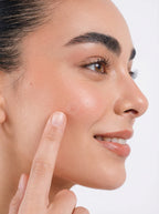Woman pointing to a blemish on her face against a white background