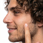 Close-up of a man with curly hair pointing to his cheek